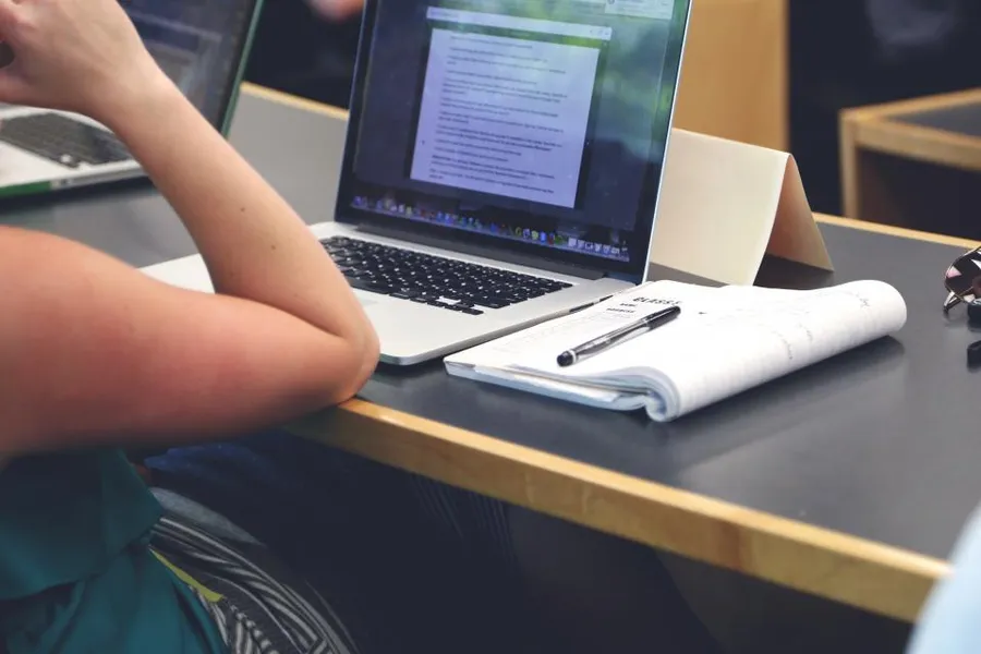 Student working on a laptop with an open notebook in a lecture room